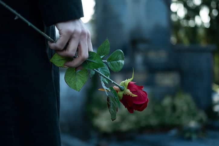 A person holding a red rose at a funeral after a wrongful death.