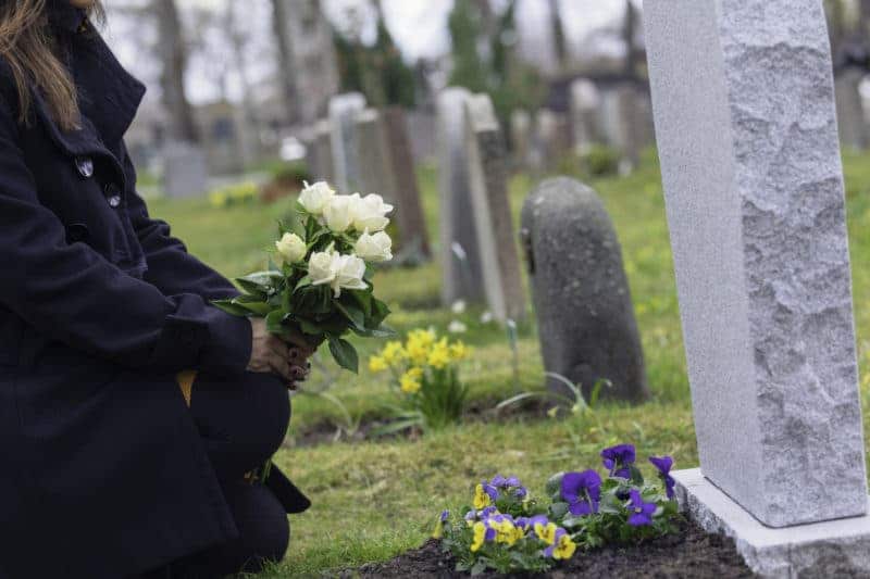 An unidentified woman holding white roses is standing in front of an unmarked tombstone.