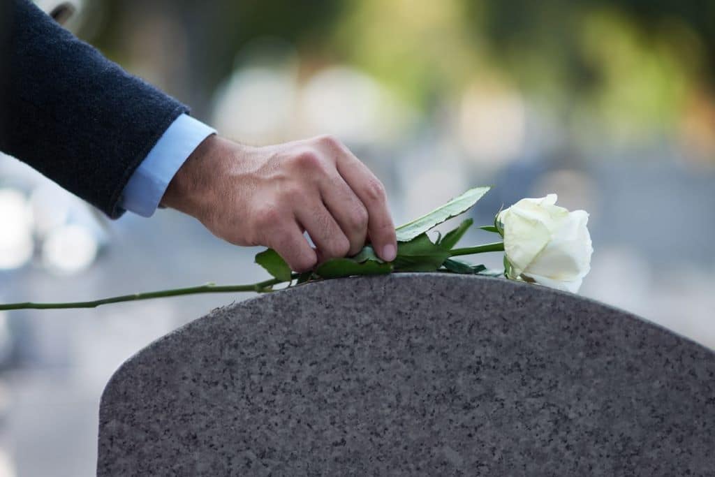 Person putting a white rose on a tombstone