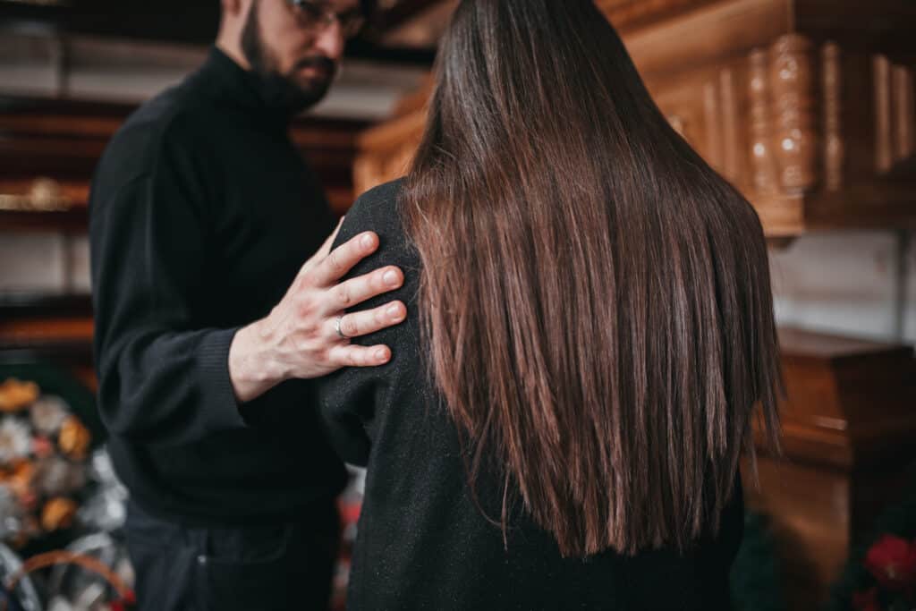 The back of a woman in distress as a man comforts her, touching her shoulder.