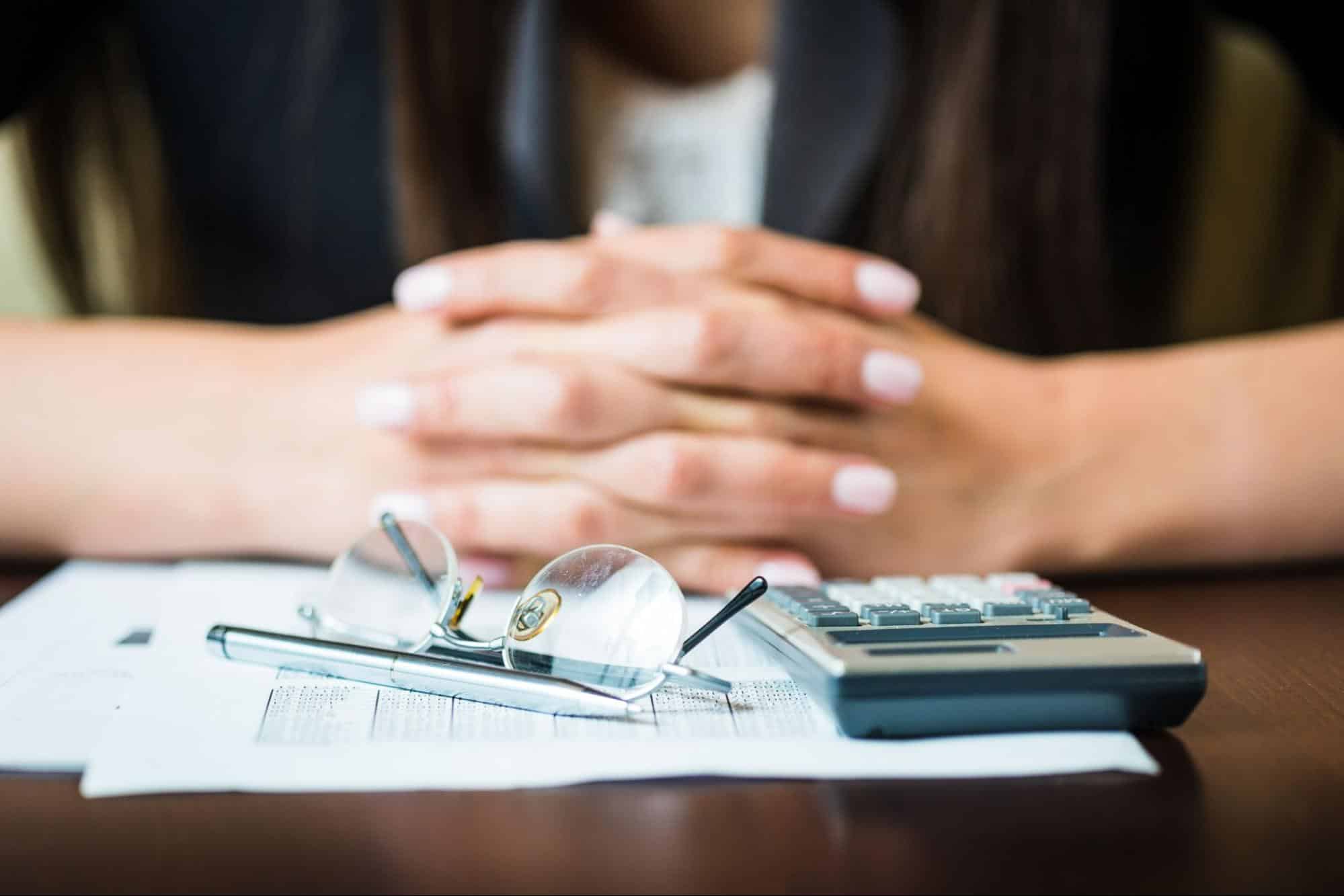 worried person with crossed hands and calculator and glasses