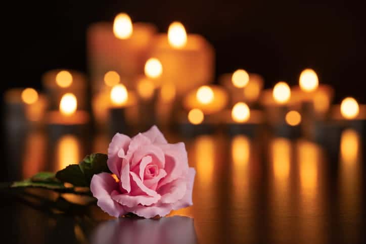 The focus is on a pink rose in front of lit candles in the background. The candles are fuzzy and out of focus.