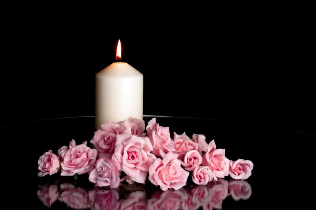 A lit white candle surrounded by pink flowers in memorial for an person who suffered a wrongful death.