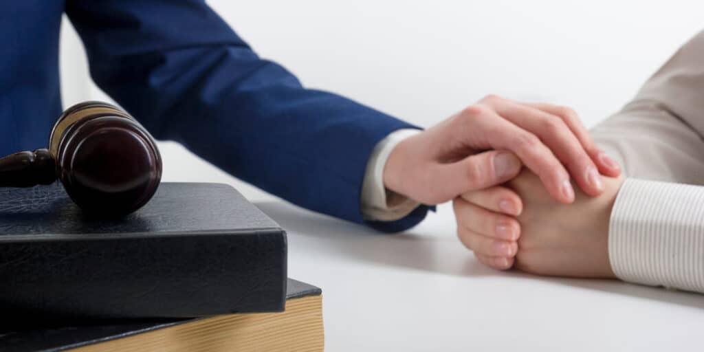 A wrongful death attorney comforting their client with their hand resting on top of theirs. On his desk is a stack of books with a gavel on top.