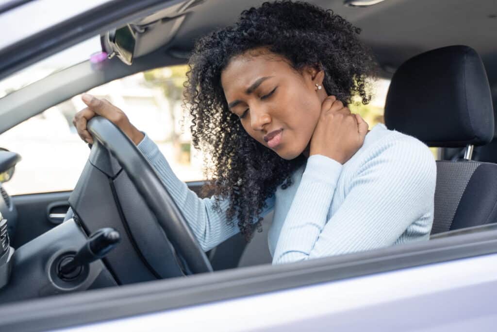 A woman holds her neck in pain while sitting behind the wheel of her vehicle after being in a car accident.