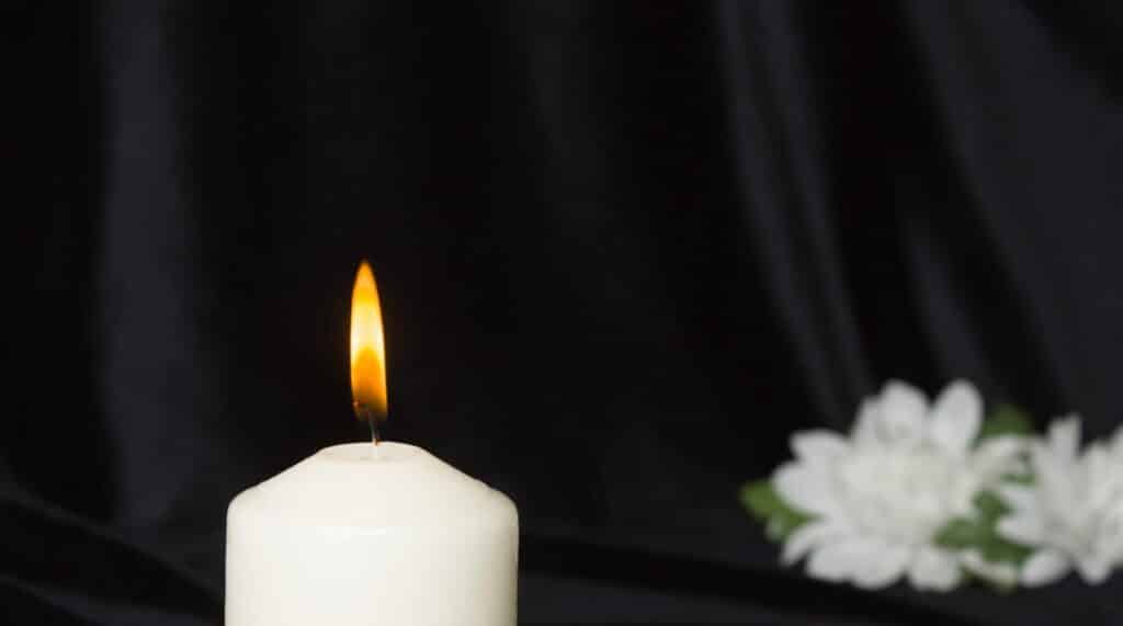 A lit memorial candle after a wrongful death with white flowers in the background.