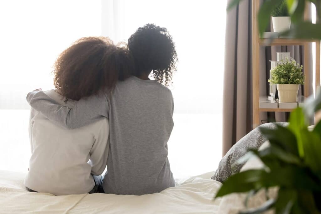 A view from the back as two women hug while sitting side by side. One offers support after a catastrophic injury.