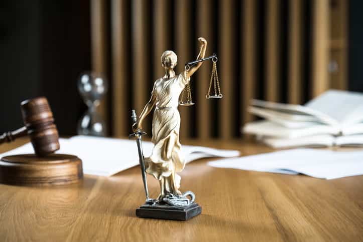 A Lady Justice statue on a catastrophic injury attorney's desk. In the background is a gavel, open books and paperwork. 