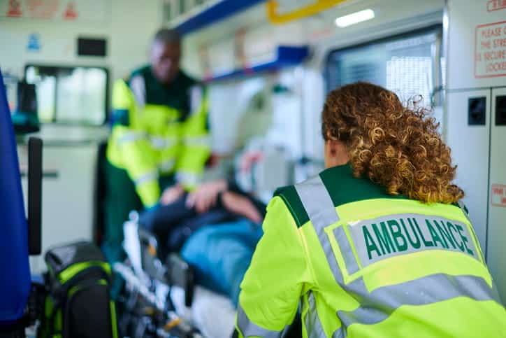 Two EMTs are helping a patient on a stretcher in the back of an ambulance after a catastrophic injury. 