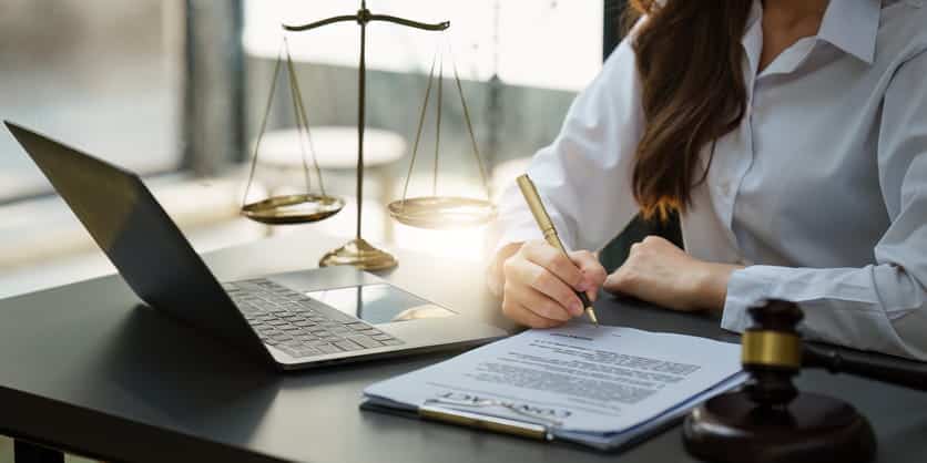 A personal injury attorney working on paperwork at her desk. In front of her is the scales of justice, an open laptop, and a gavel. 