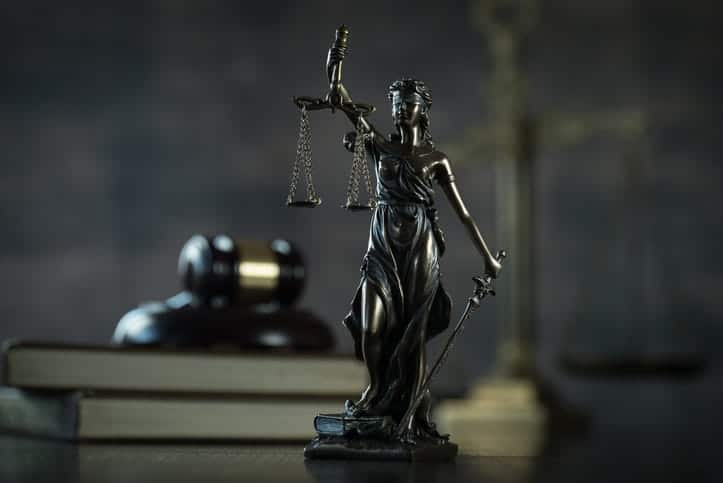 A Lady Justice statue in front of a stack of books with a gavel on top. 