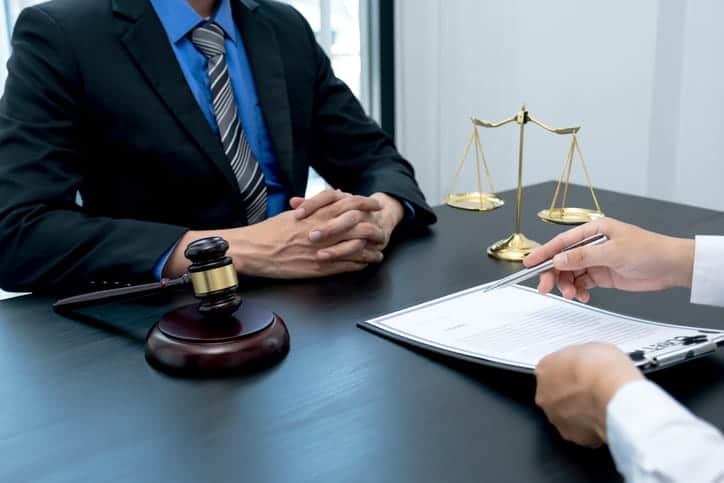 A wrongful death attorney reviews a contract with a client. Next to them is the scales of justice and a gavel. 