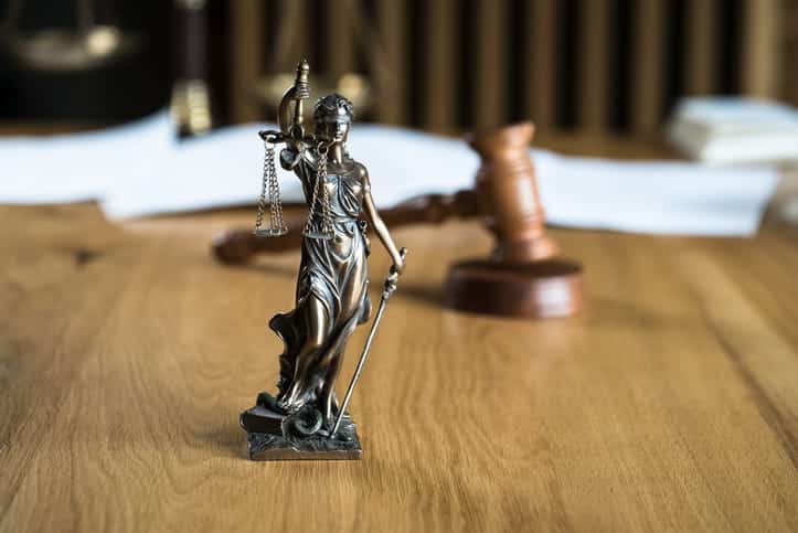 A Lady Justice statue with a gavel and paperwork behind it. 