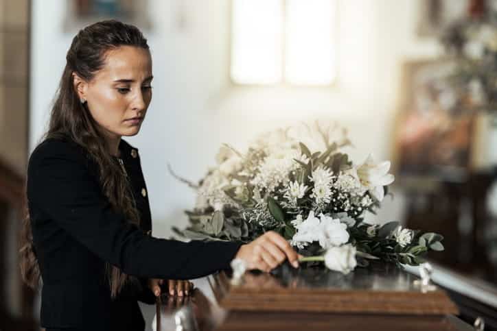 A woman in mourning placing a flower on a casket. 